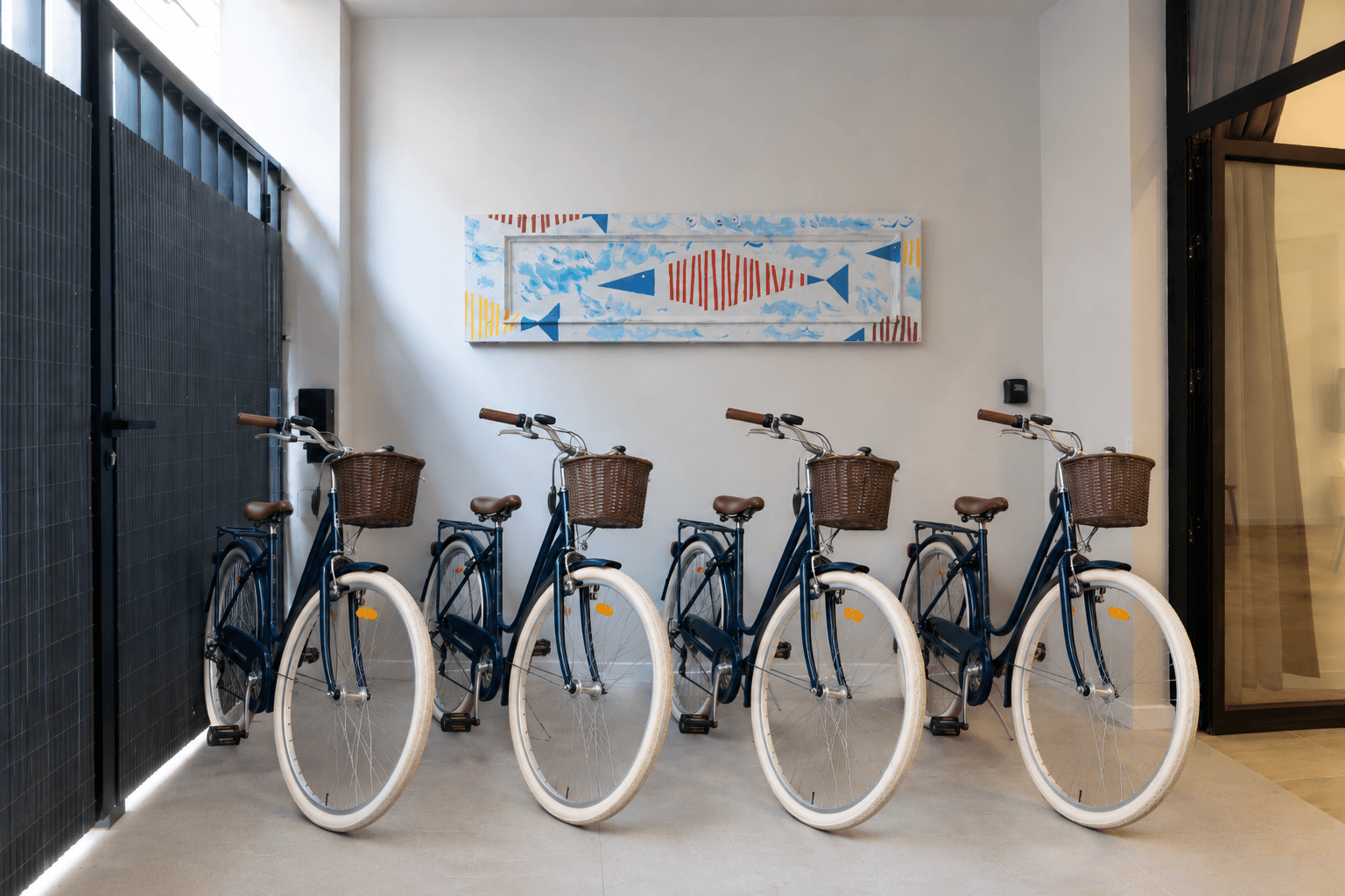 Cuatro bicicletas urbanas azules con cesta de mimbre, aparcadas en el portal del edificio